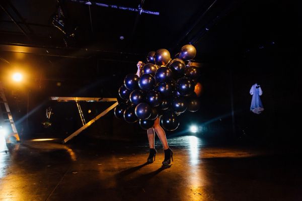 Person obscured by cluster of black balloons in dark room.