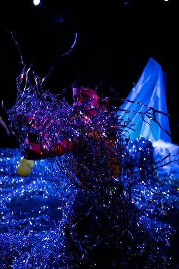 Person entangled in glowing blue streamers in dark setting.