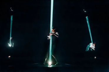 Three people illuminated by narrow beams of light on a dark stage.