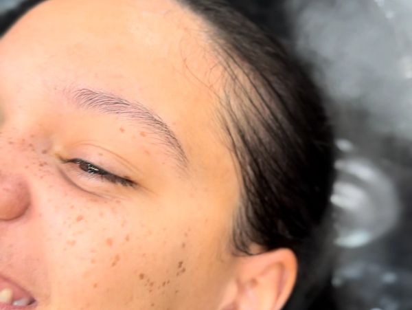 Close-up of a woman with freckles smiling at a salon sink.