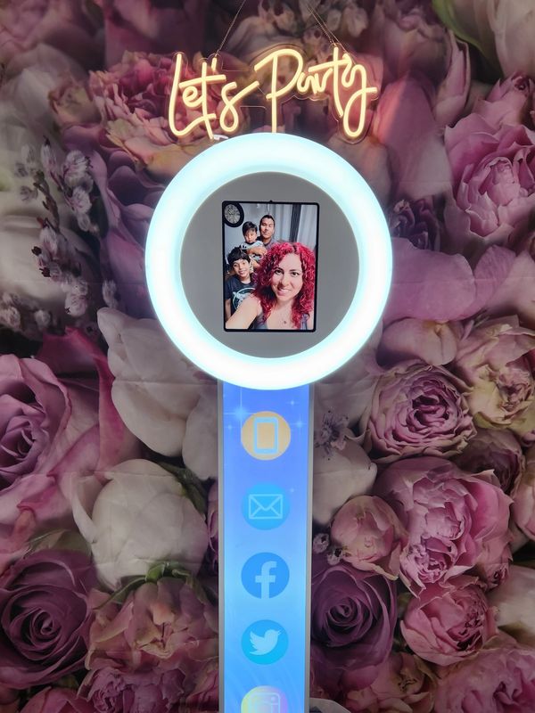Photo booth with a floral backdrop and neon 'Let's Party' sign.