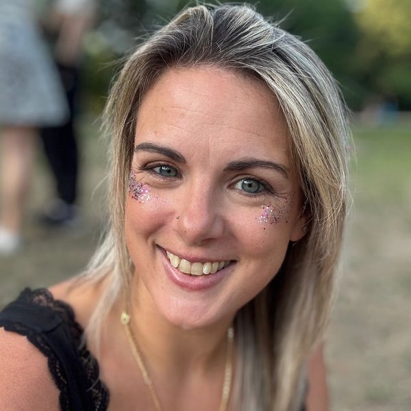 Smiling woman with glitter makeup on cheeks in an outdoor setting.