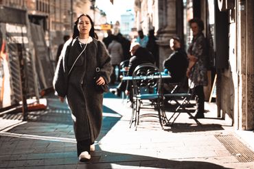 Woman in a long coat walking down a sunlit city street.
