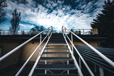 Metal staircase leading upwards against a cloudy sky.