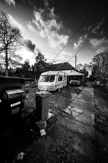 Black and white photo of a driveway with a caravan and car under a carport.