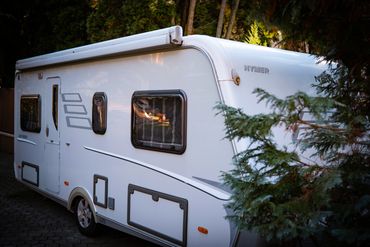 White Hymer camper parked beside trees in a serene setting.