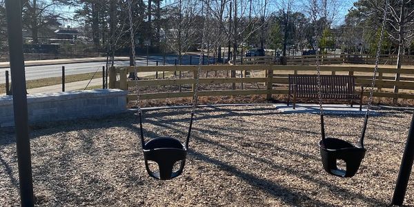 Toddler swings surrounded by soft mulch surface in need of playground inspection