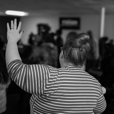 Woman with striped shirt raising her hand in a crowd.
