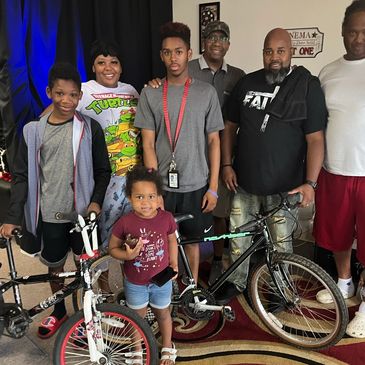 A group of six people posing with bicycles indoors.