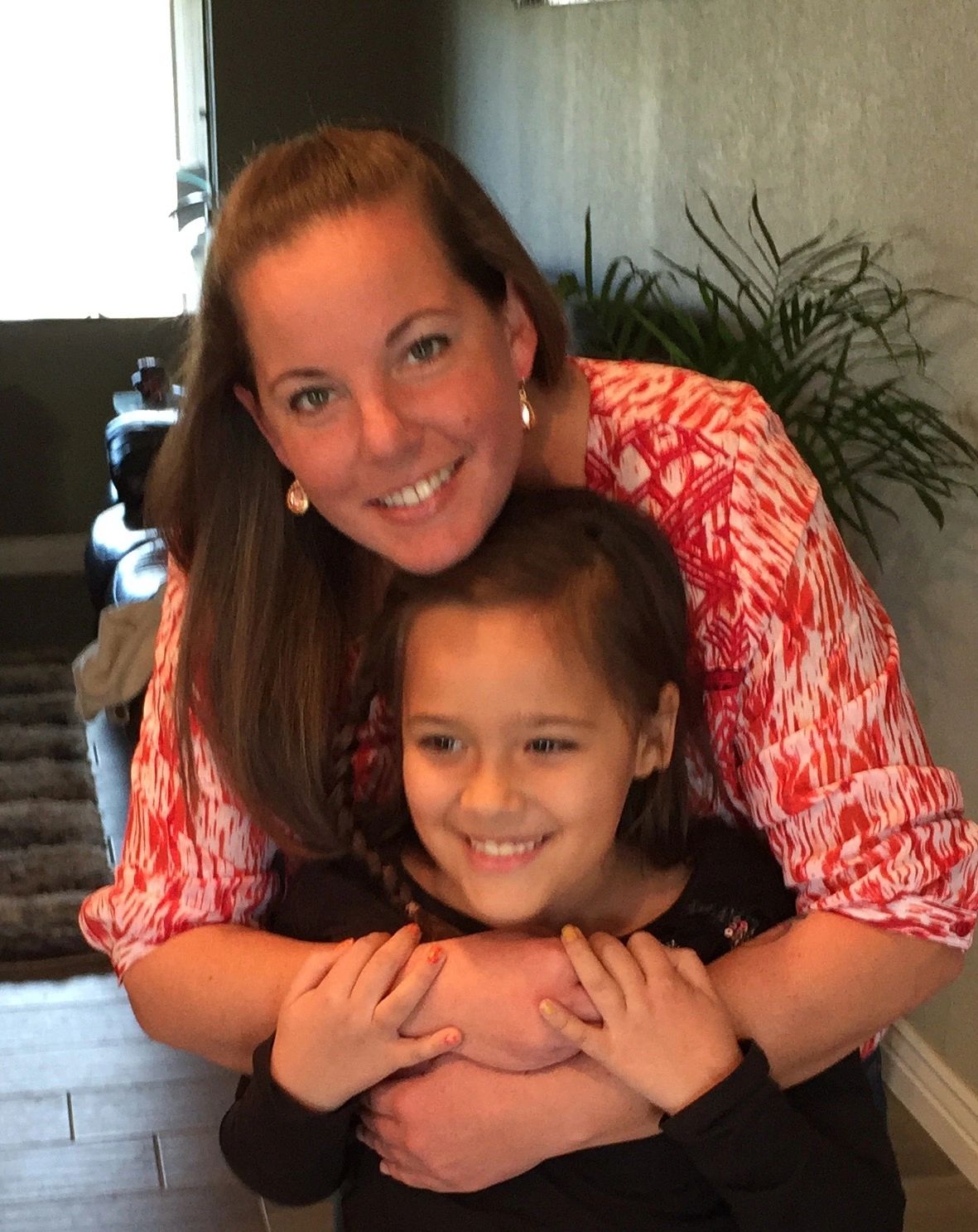 A woman warmly hugging a smiling young girl indoors.