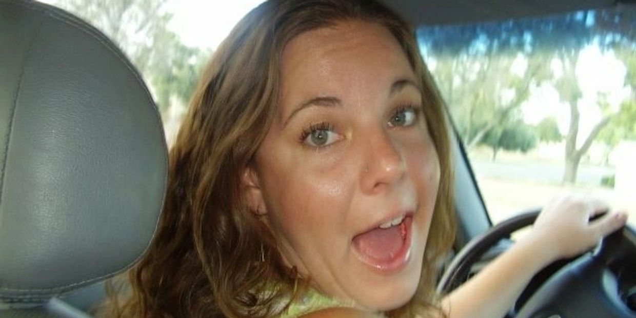 A woman driving a car with a joyful expression, looking back.