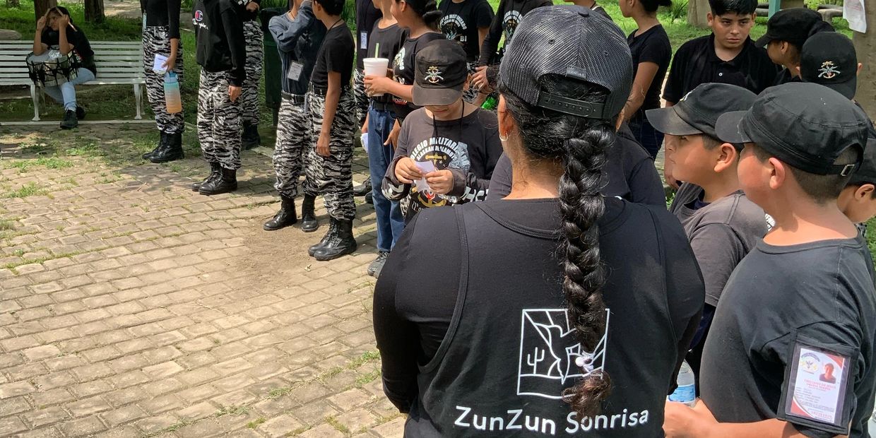 Group of people, mostly kids, dressed in black with some in camouflage pants, gathered outdoors.