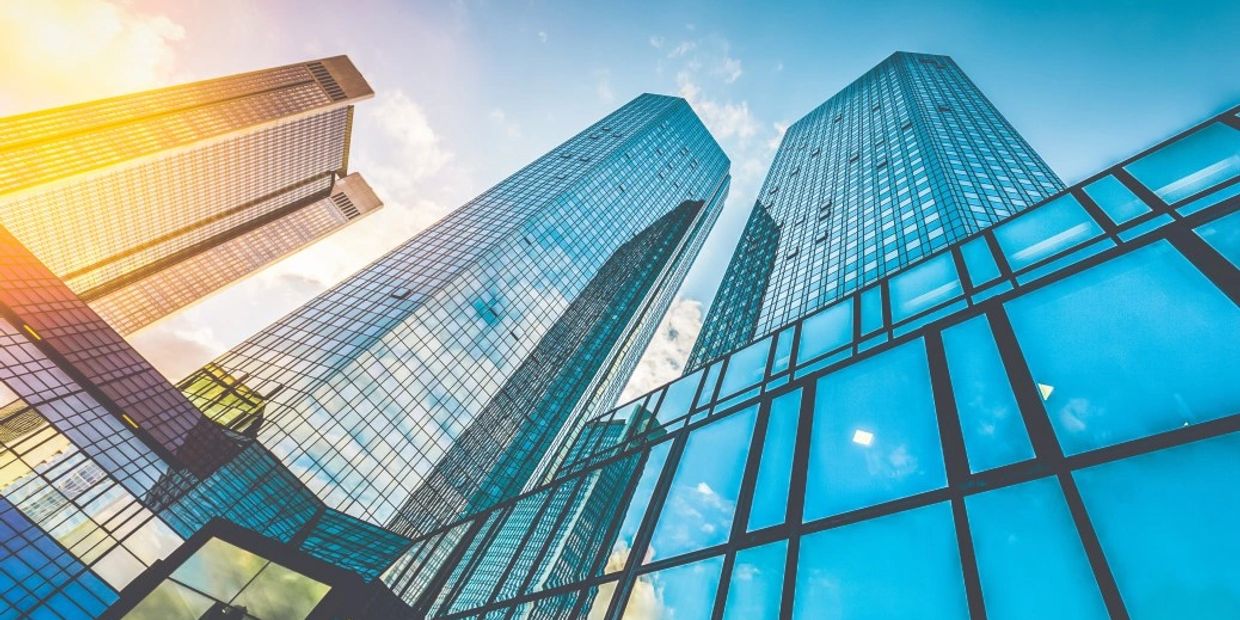 Sunlit glass skyscrapers towering into a clear blue sky.