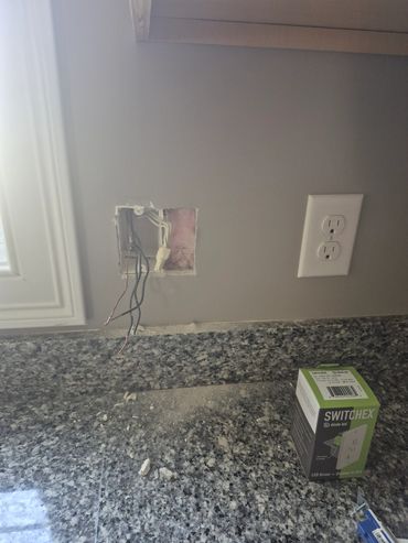 Kitchen wall with exposed wiring and an outlet.