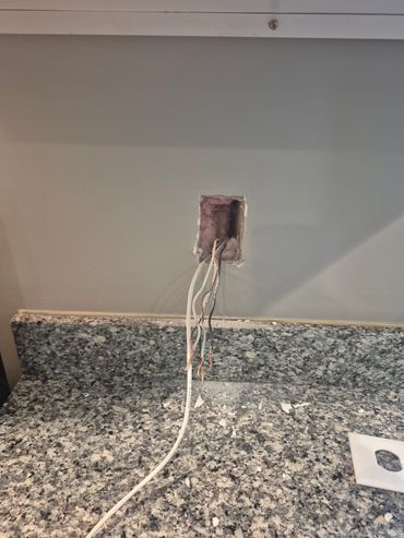 Electrical wires protruding from a wall outlet above a granite countertop.