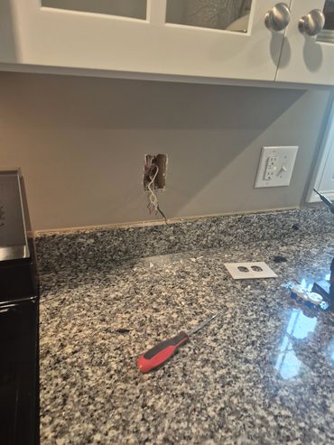Open electrical outlet on kitchen wall with tools nearby.
