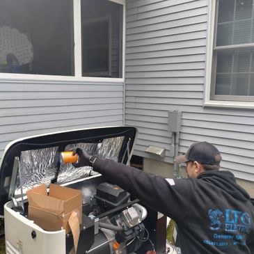 Technician working on an outdoor generator under a house window.
