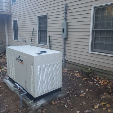 Outdoor Generac generator installed beside a house with fallen leaves around.