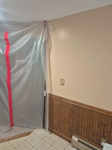 Plastic sheet with red tape covering door opening in a room with wood paneling.