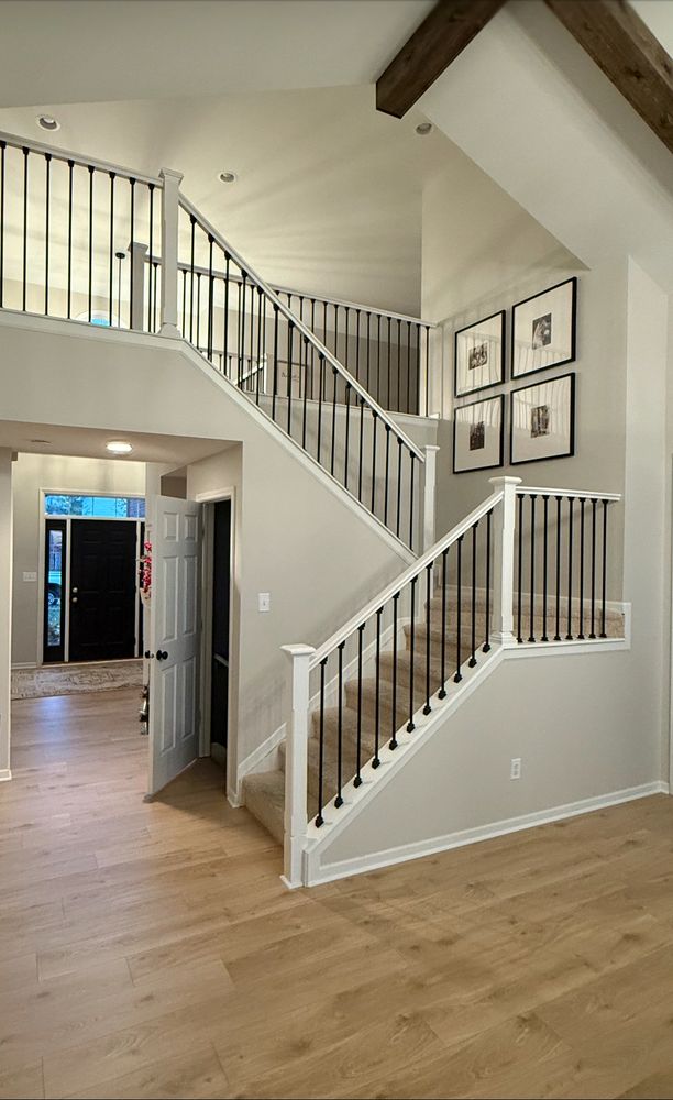 Modern staircase with black railings and light wood flooring in a bright home entryway.
