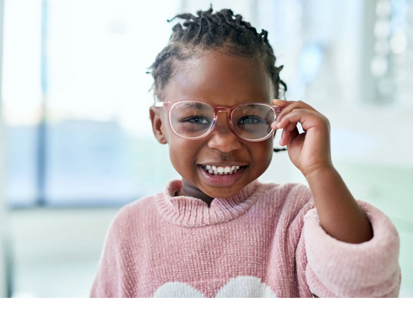 Smiling child adjusting pink glasses, wearing a cozy pink sweater.