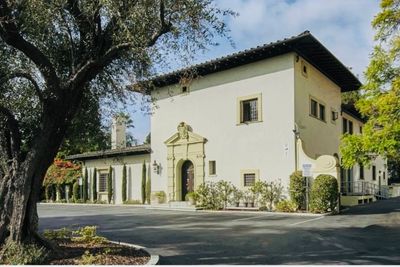 A charming Mediterranean-style house surrounded by trees and a driveway.