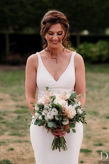 Bride in a white dress holding a flower bouquet, smiling.