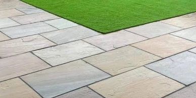 Neatly arranged light-colored stone tiles adjacent to a green artificial grass patch.