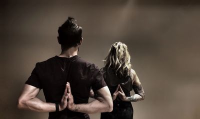 Two people practicing yoga with hands in reverse prayer pose against a neutral background.
