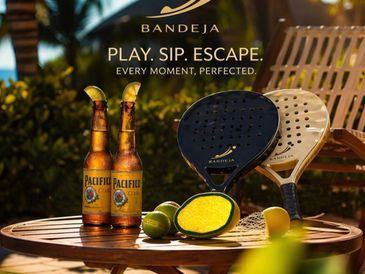 Two beers, paddle tennis rackets, and limes on a table outdoors at sunset.