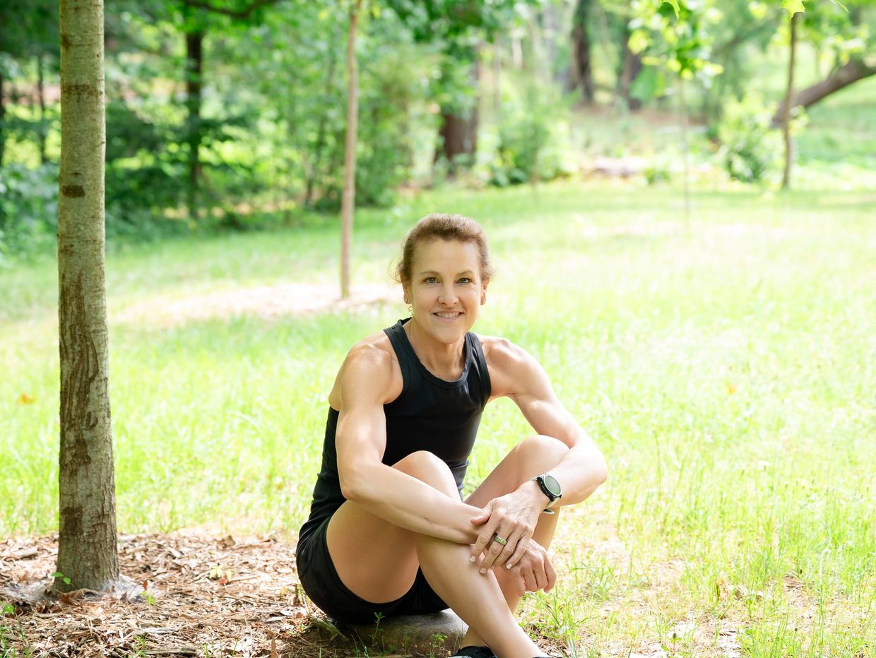 Fit woman in black athletic wear sitting outdoors on grass, smiling.
