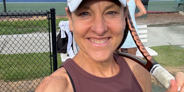 Smiling woman in tennis attire holding a racket on a court.