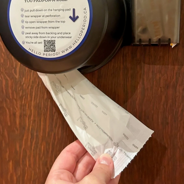 Menstrual Pad pulled down and displayed from the Pads-on-a-Roll dispenser installed on a wall