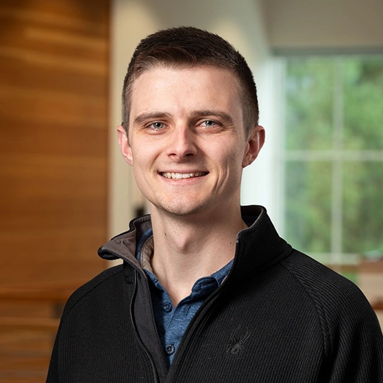 Smiling young man in a casual jacket with a blurred indoor background.