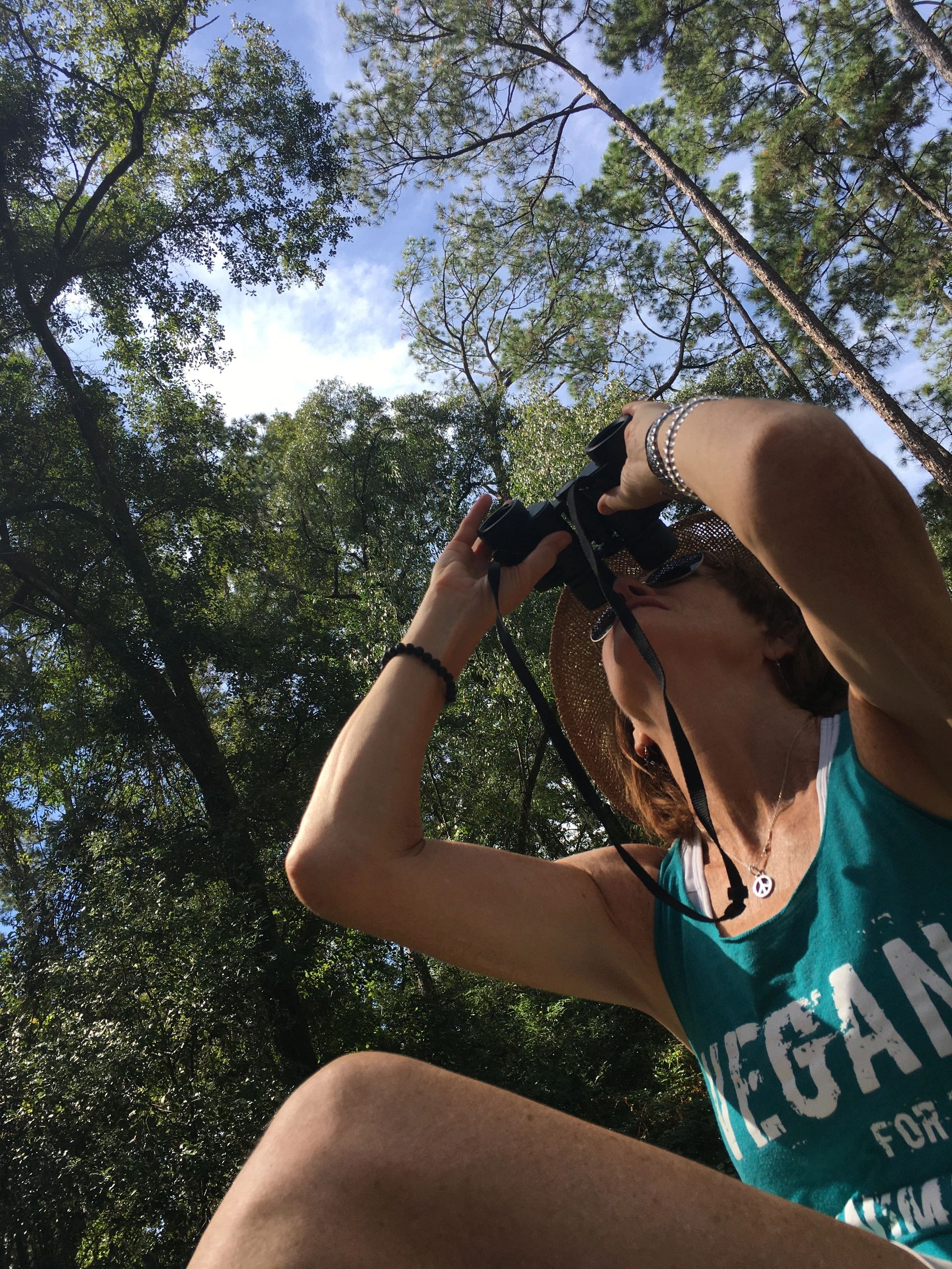 Person in a hat using binoculars in a forest.