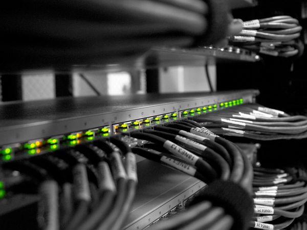 Network switch with glowing green LED lights and connected Ethernet cables.