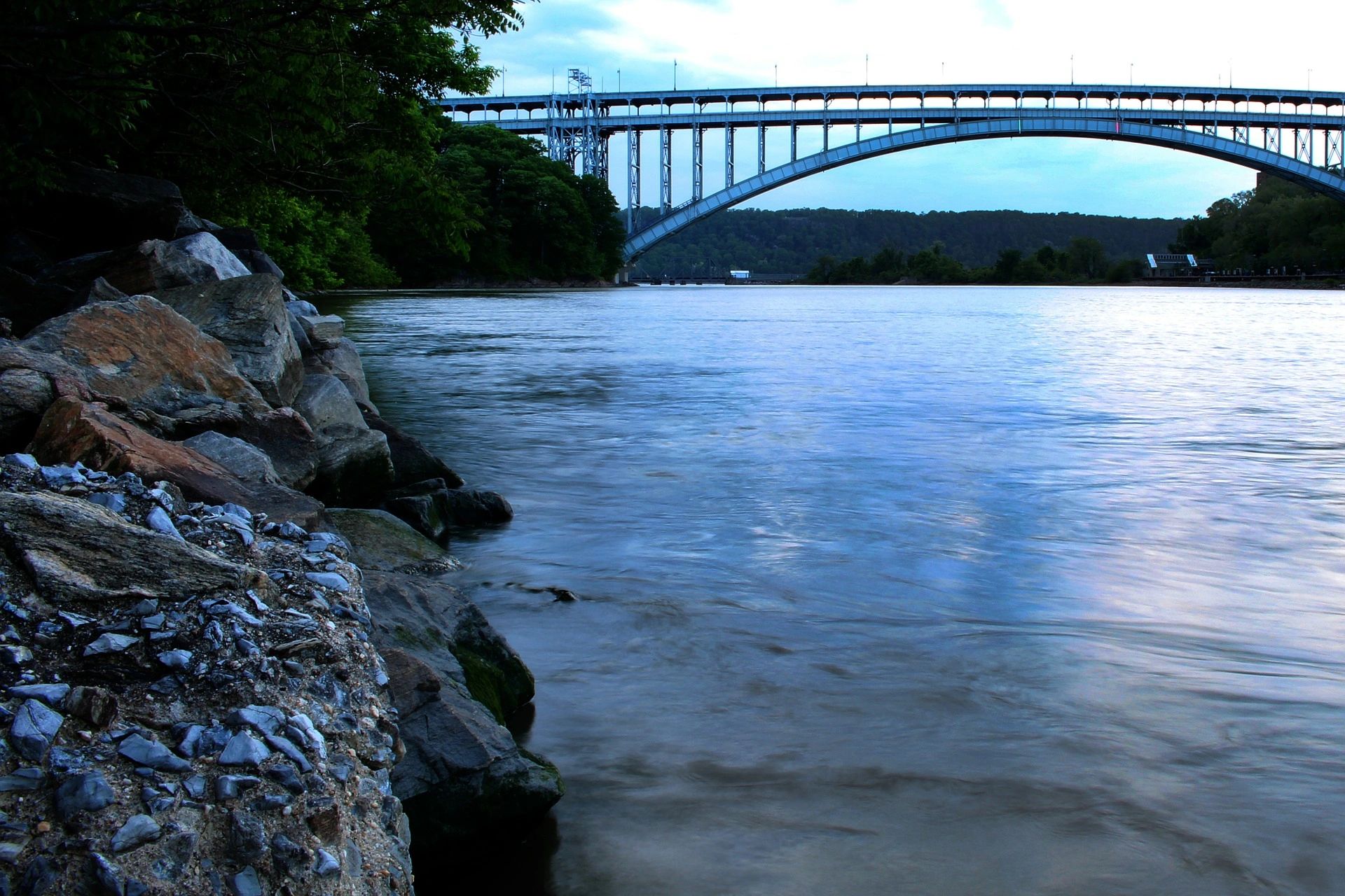 Henry Hudson Bridge over Hudson River with rocky shore in front left of image