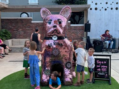 Children playing around a shiny dog sculpture that says 'Be Kind'.