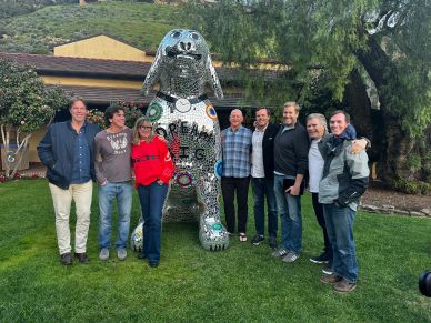 Group of eight people posing with a large mosaic dog statue outdoors.