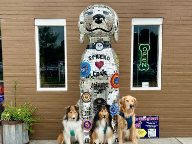 Three dogs sitting in front of a large dog sculpture.
