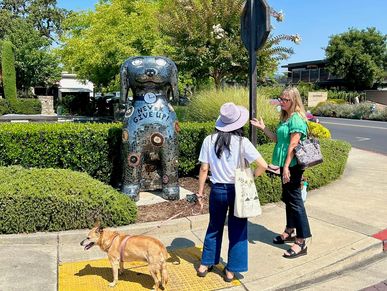 Two women and a dog near a colorful dog statue with "Never Give Up".