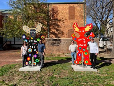 Four people stand next to colorful sculptures with positive messages.
