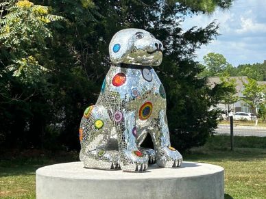 Mosaic sculpture of a sitting dog outdoors.
