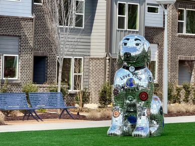 Large mosaic dog sculpture on grass near benches.