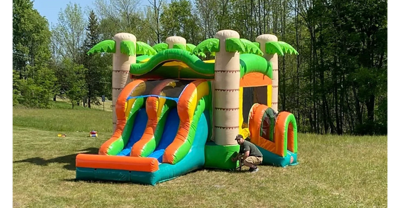 Colorful bounce house with two slides rests in a green field.