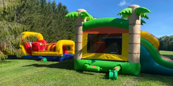 Two colorful bounce houses sit side by side in a green field on a sunny day. 