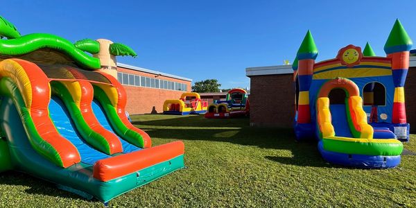Two bounce houses with slides facing each other on a field of grass.