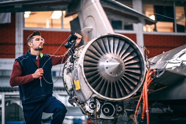 Aircraft engineer in safety glasses and vest inspecting a jet engine in a hangar