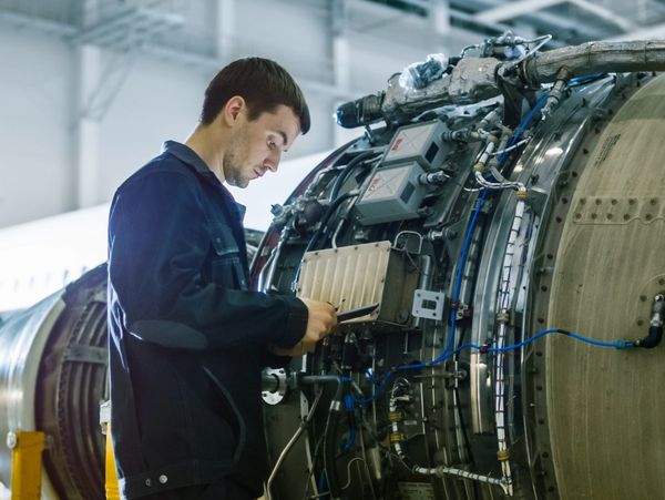 Man in a work jacket inspecting complex machinery, possibly a jet engine