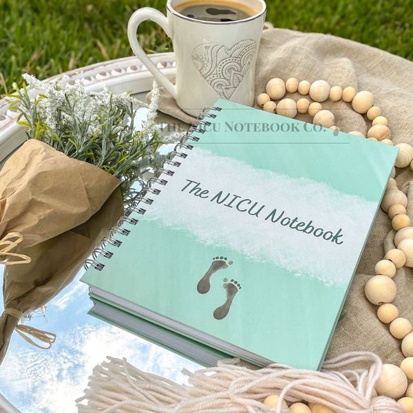 Photo of The NICU Notebook displayed on a mirror outdoors with a cup of coffee and flowers.